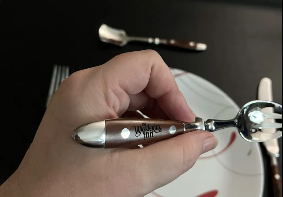Close-up of the spork held in one hand, showing The Wandering Inn logo laser-engraved into the wooden handle