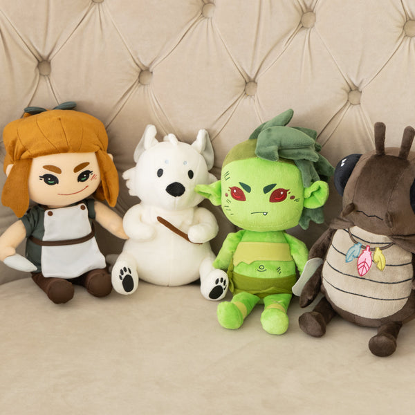 Four plushies sitting against a wall, from left to right, Erin Solstice plushie, Mrsha plushie, Rags plushie and Bird plushie