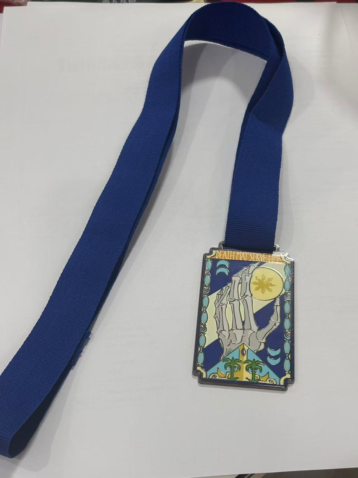 Khelt medallion featuring a skeletal hand reaching for the sun, on its blue lanyard