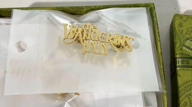The Wandering Inn logo lapel pin in gold-plated stainless steel, the series wordmark cut as a single piece