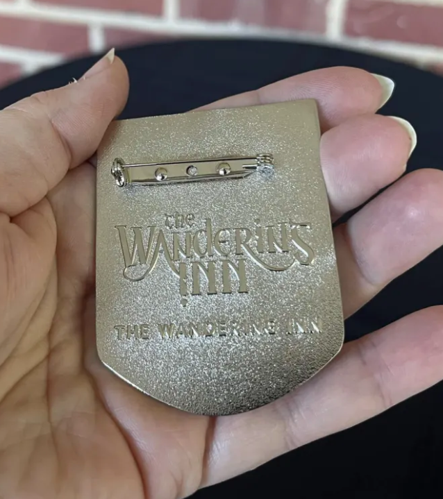 Reverse of the Liscor City Watch badge: pin fastening and The Wandering Inn logo raised on the textured metal back