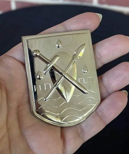 The Liscor City Watch badge in hand, angled to show the polished relief of the sword, spear and waves
