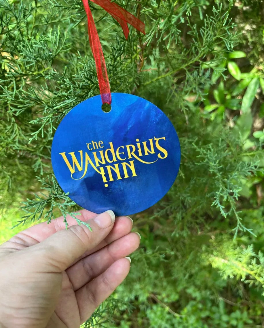 The Wandering Inn Christmas ornament hanging on a tree, logo side, red ribbon