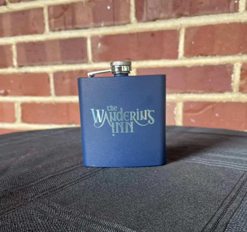 The Wandering Inn stainless steel hip flask standing upright, navy finish with logo