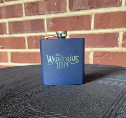 The Wandering Inn stainless steel hip flask standing upright, navy finish with logo
