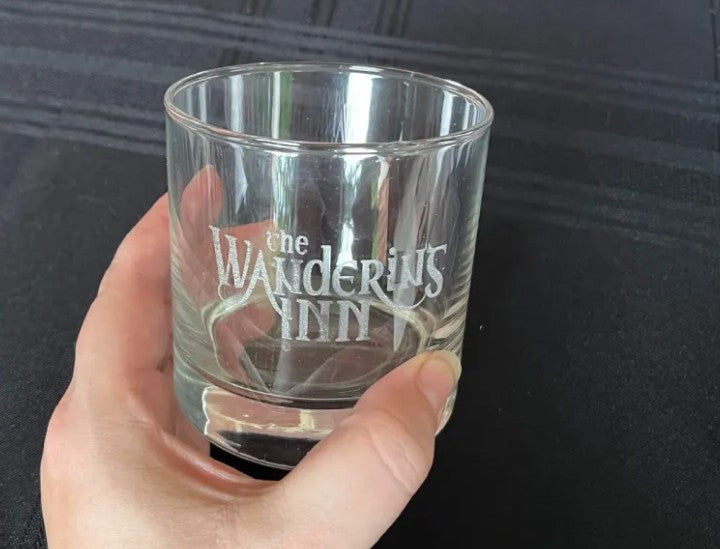 Glass held in a hand, etched logo crisp against a dark background