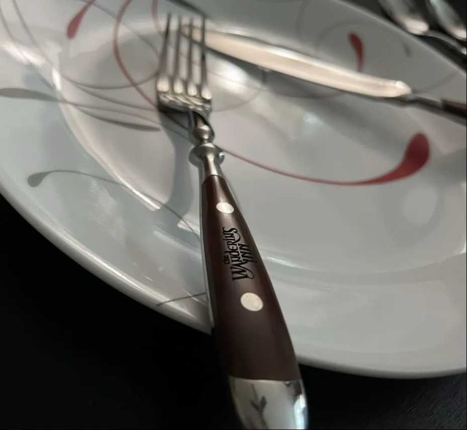 Dinner fork resting on a plate, with The Wandering Inn logo engraved on the wooden handle in detail