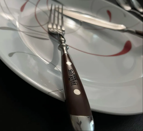 Dinner fork resting on a plate, with The Wandering Inn logo engraved on the wooden handle in detail