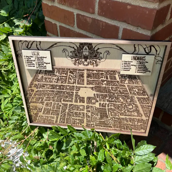 Decorative map with text and design elements on a wooden board, placed outdoors against a brick wall.