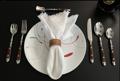 Six-piece Wandering Inn cutlery set laid out around a plate: dinner fork, dinner knife, large spoon, small spoon, spork and butter spreader, each with a dark wooden handle and stainless steel head