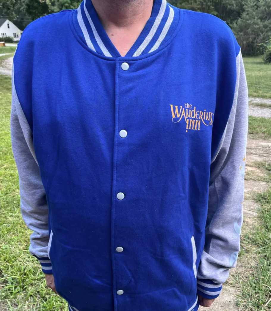 The Wandering Inn letterman jacket worn, royal blue body with heather gray sleeves and the series wordmark on the chest