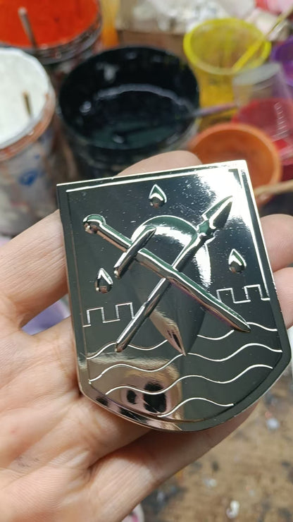 The Liscor City Watch badge angled to catch the light, showing the raised relief of the crossed sword and spear and the polished silver plating